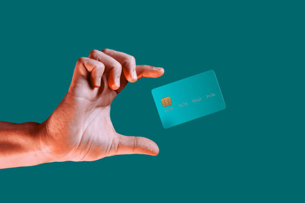 Una mano acercándose a alcanzar una tarjeta de crédito que flota en un fondo azul verdoso